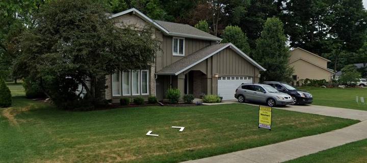 Original listing photo of the house from the street, with two cars in the driveway and a real estate sign on the lawn