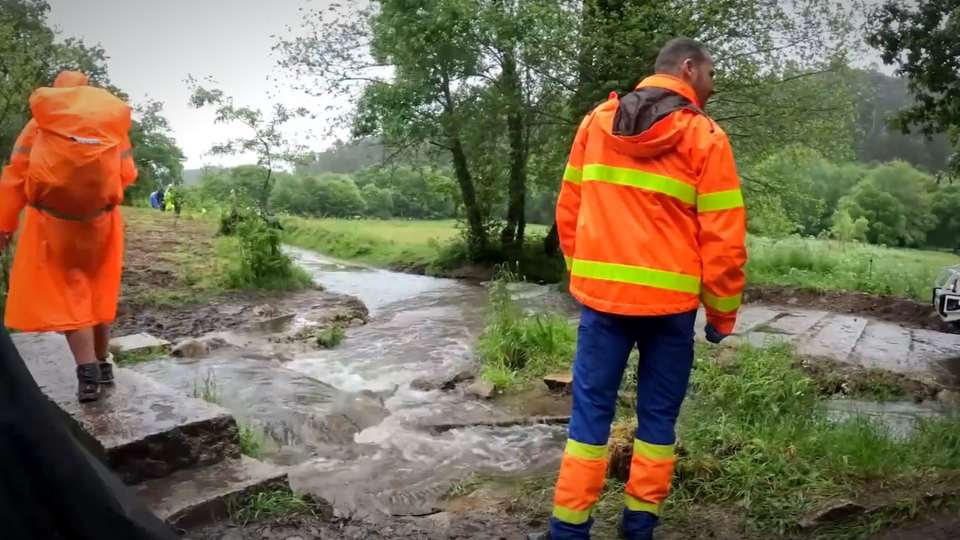 Two pilgrims in rain ponchos walking a flooded, muddy path