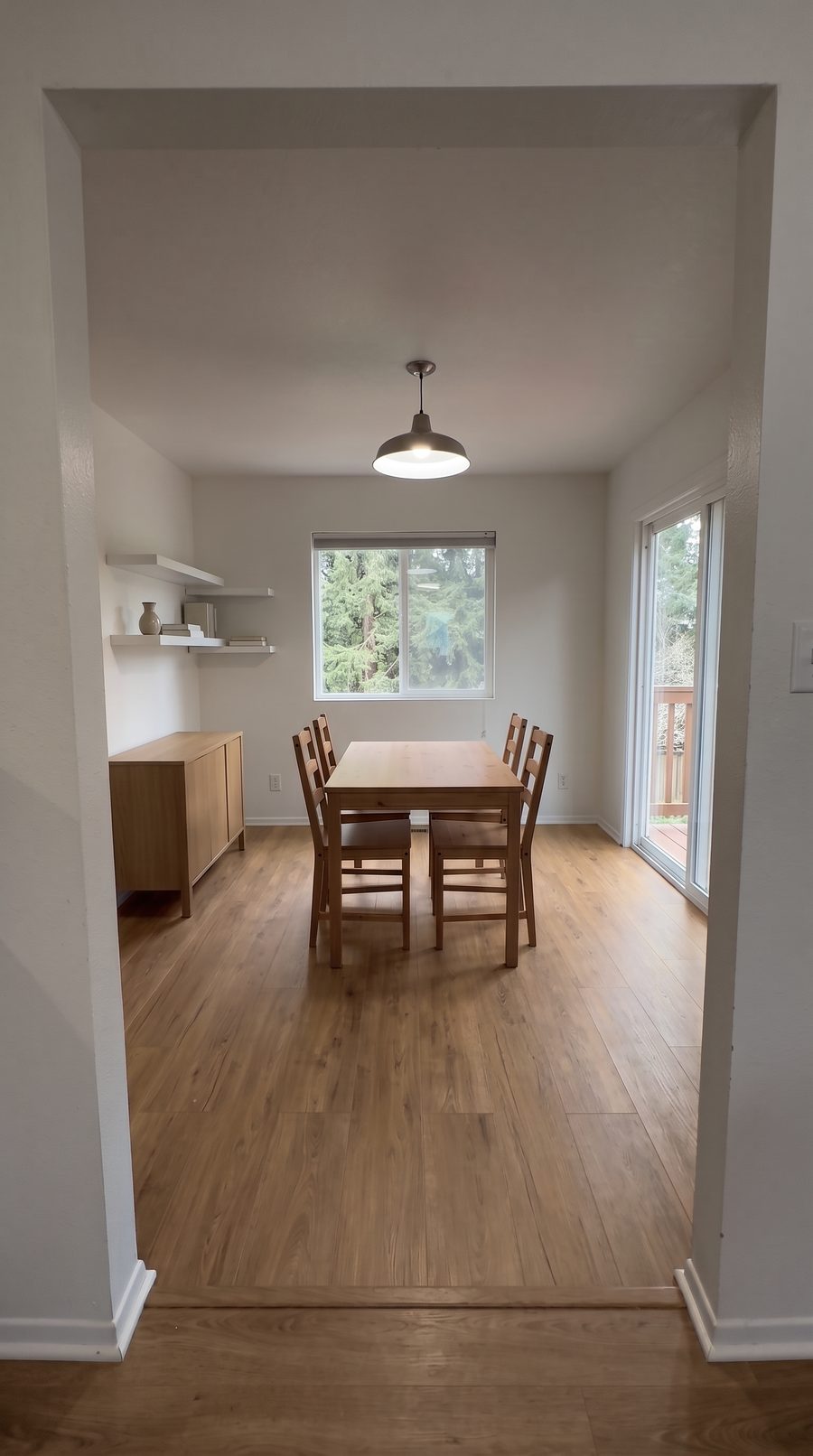 The dining room virtually staged: a simple wood table and chairs under the single pendant light, sideboard to the left, sliding door to the right, the doorway and floor as filmed